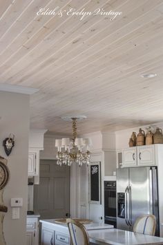 a chandelier hanging from the ceiling in a kitchen with white cabinets and appliances