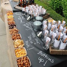 a long table topped with lots of food and drinks on top of a sidewalk next to bushes