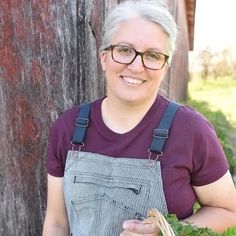 a woman holding a basket full of greens and smiling at the camera while standing next to a tree