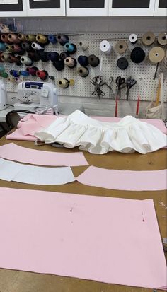 two pieces of pink paper sitting on top of a wooden table next to sewing supplies