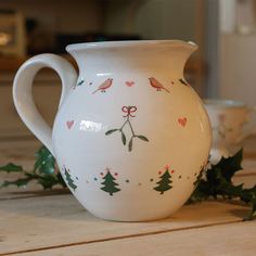 a white pitcher sitting on top of a wooden table next to holly and christmas decorations