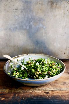 a bowl filled with green vegetables on top of a wooden table