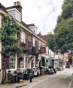 people are sitting at tables in front of a restaurant on the side of a street