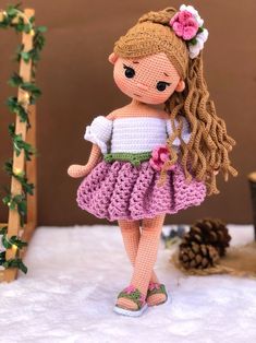 a crocheted doll is standing in the snow wearing a dress with flowers on it