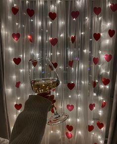 a person holding a wine glass in front of a window with hearts on the curtain