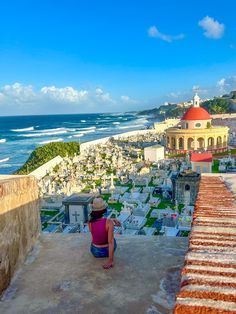 a woman sitting on top of a roof looking at the ocean and buildings in front of her