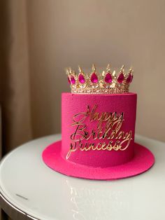 a pink birthday hat with gold lettering and a crown on top is sitting on a table