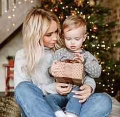 a woman holding a small child in front of a christmas tree