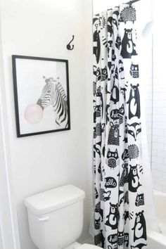 a white toilet sitting next to a bath tub in a bathroom with black and white shower curtain