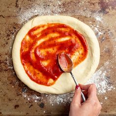 someone is spreading sauce on a pizza dough