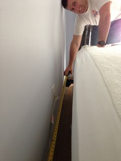 a man measuring the length of a bed with a tape measure in his left hand