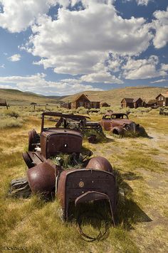 old rusted out cars sitting in the middle of a field with grass and buildings