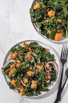 two white plates filled with salad on top of a marble table next to silverware