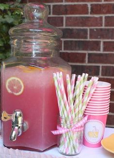 a beverage dispenser filled with pink lemonade and straws on a table