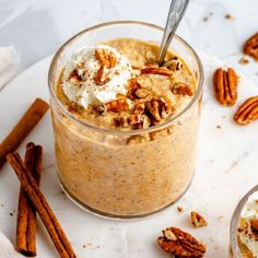 a dessert in a glass with whipped cream and pecans around it on a white plate