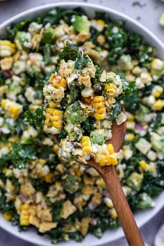 a wooden spoon filled with corn salad on top of a white plate next to other food