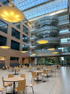 an indoor dining area with tables and chairs in front of a large glass ceilinged building