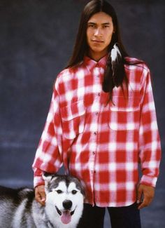 a man standing next to a husky dog wearing a red and white checkered shirt