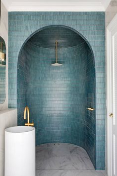 a bathroom with blue tile and gold fixtures in the shower area, along with a white pedestal sink