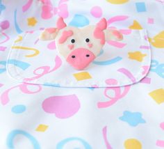 a close up of a pink and white cow brooch on a blue and yellow blanket