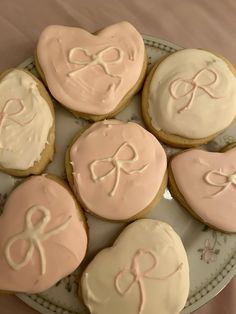 six decorated cookies on a plate with pink icing in the shape of heart and bow