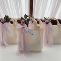 three bags with pink flowers and ribbons tied to them on a table in front of white drapes