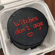 a black cake with red writing on it sitting in a white box that says witches don't age