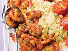 shrimp, rice and tomatoes on a white plate with silver serving utensils next to it