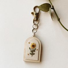 a keychain with a sunflower embroidered on the front and back, hanging from a metal hook