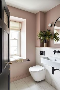 a white toilet sitting next to a window in a bathroom under a mirror with a potted plant on top of it