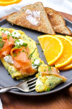 an omelet with salmon, bread and orange slices on a plate next to a fork