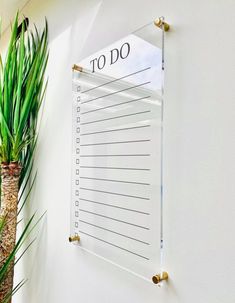 a clear to do list hangs on the wall next to a potted plant and a palm tree