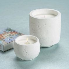 two white candles sitting on top of a table next to a boxed book and candle holder