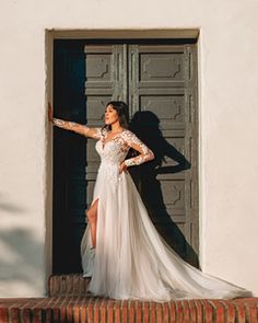 a woman standing in front of a door wearing a white dress and holding her arms out