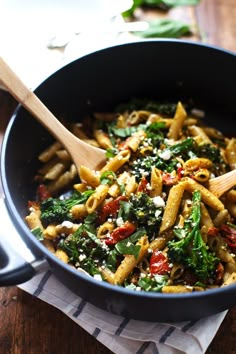 a skillet filled with pasta, spinach and tomatoes