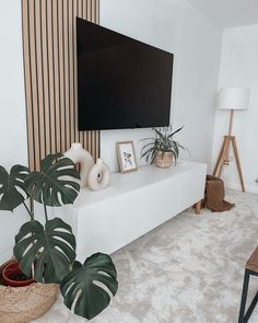 a flat screen tv sitting on top of a white shelf next to a potted plant