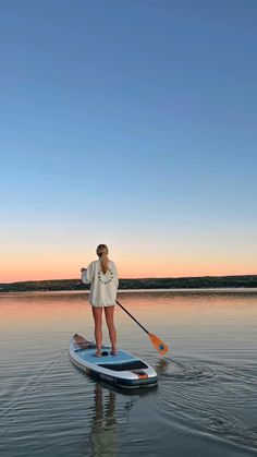 a woman standing on top of a paddle board in the water at sunset or dawn