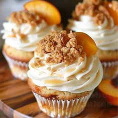 cupcakes with white frosting and peaches on a wooden platter, ready to be eaten