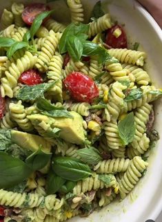 a pasta salad with spinach and tomatoes in a white bowl on a wooden table