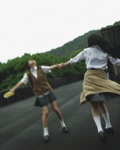 two women in school uniforms are playing with a frisbee on a road near some trees