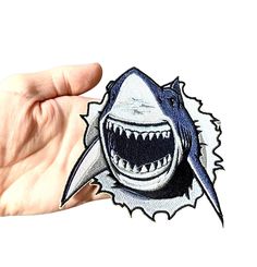 a hand holding up a sticker with a shark on it's face and teeth