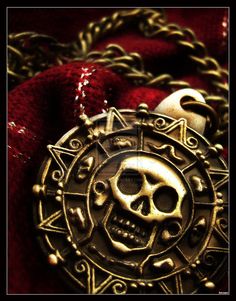 a skull and crossbones pendant on a red cloth with gold chains around it