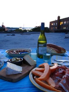 a table topped with lots of food next to a bottle of wine and two plates filled with meats