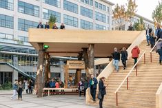 many people are walking up and down the stairs in front of a building with large windows