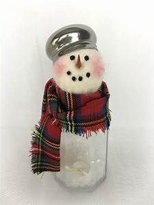 a glass jar with a snowman in it and a scarf around its neck, sitting on a white surface