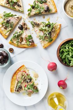 several slices of pizza sitting on top of a white plate next to olives and radishes