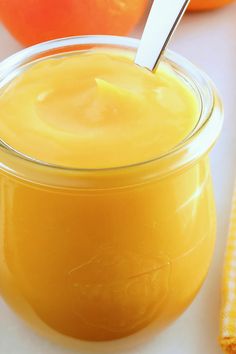 an orange juice in a glass jar with a spoon sticking out of it next to some oranges