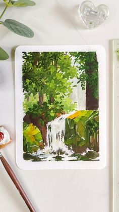 a watercolor painting of a waterfall in the woods next to some paintbrushes