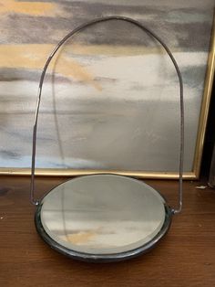 a round mirror sitting on top of a wooden table next to a wall hanging frame