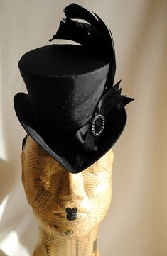 This gothic victorian mini top hat is an excellent choice for any dark cabaret event. It is covered with taffeta and embellished with various black trimmings. Two curled black rooster feathers, ribbons, a silver and black rhinestone round buckle and a just a hint of black veil. Choose between total black(pictured),blue or burgundy with black decoration. Measurements : height 4 inches( 10 cm ) front to back 9 inches ( 22 cm ) side to side 7.5 inches ( 19 cm ) This mini top hat is fully lined with Punk Top Hat For Halloween Party, Black Gothic Hat For Costume, Gothic High Crown Costume Hat, Punk Style Top Hat For Halloween Party, Punk Style Halloween Party Top Hat, Witchy Brimmed Costume Hats For Parties, Black Halloween Top Hat With Short Brim, Vintage High Crown Top Hat For Costume Party, Steampunk Top Hat With Curved Brim For Costume